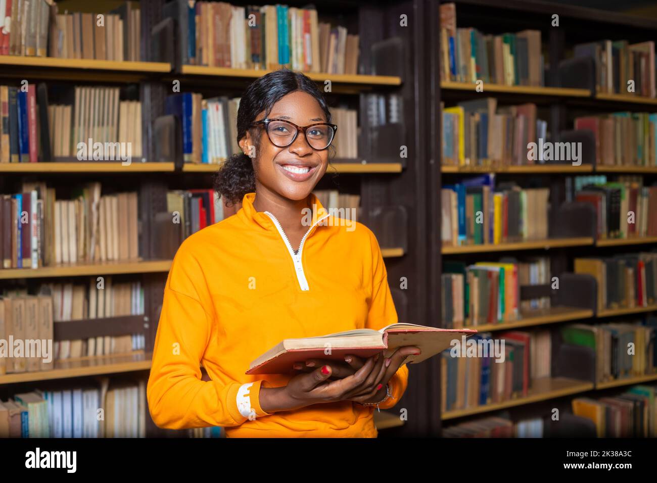 A Black female student holding a red book and standing in the college ...