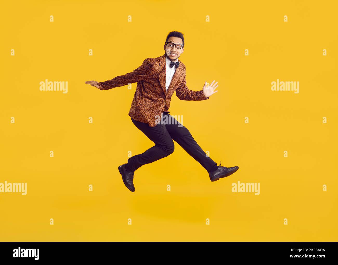 Cheerful funny dark-skinned young man in leopard jacket having fun jumping on yellow background. Stock Photo