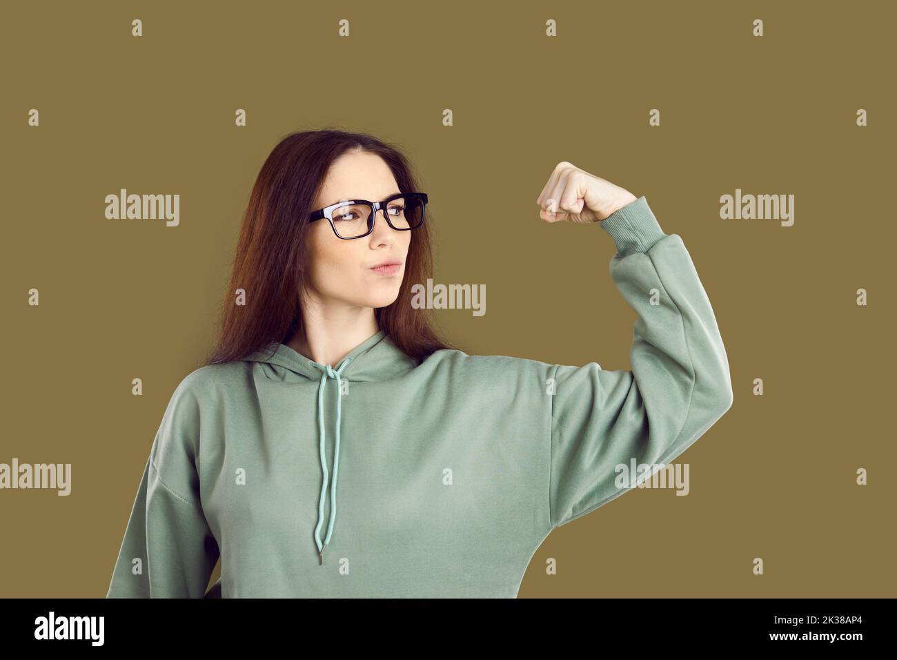 Confident strong young girl flexing her arm and showing her power isolated on brown background Stock Photo