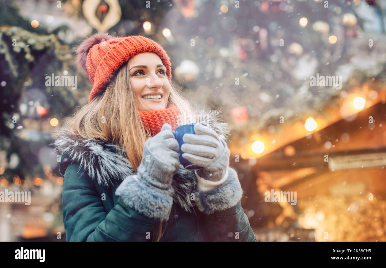 Woman in front of Christmas tree on winter market drinking hot wine Stock Photo