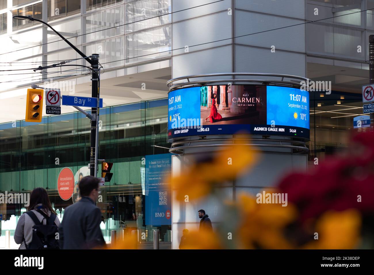 A Bay St. street sign is seen at the base of BMO's First Canadian Place in Toronto Financial District. as people walk by a TSX digital ticker sign. Stock Photo