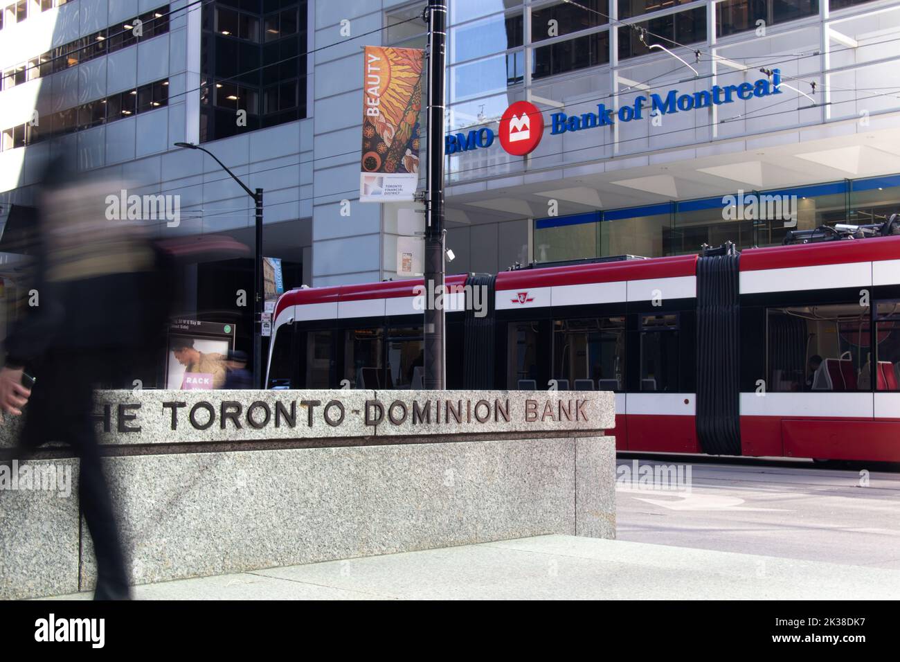 A TTC streetcar passes by the base of BMO's First Canadian Place as a businessman, blurred, walks by a TD Bank sign in Toronto Financial District. Stock Photo