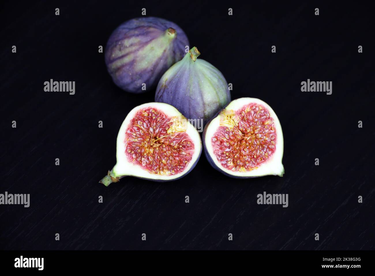 Ripe figs, half cut and whole fruits on dark wooden table Stock Photo
