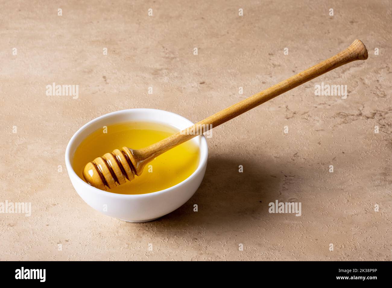 A bowl of honey and a wooden spoon for honey on a light surface. Selective focus. Stock Photo