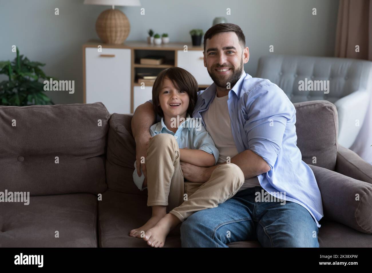 Happy dad and cheerful little son boy sitting on sofa Stock Photo