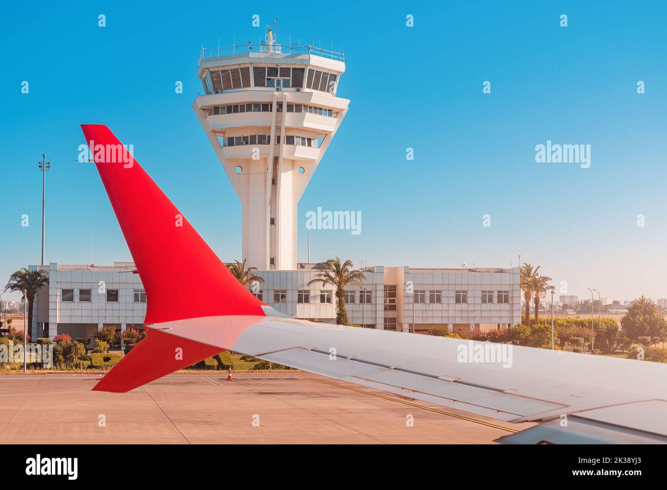 Wing of airplane and a control tower at the airport serving safe takeoffs and landings of aircraft. Runway infrastructure and dispatch work Stock Photo