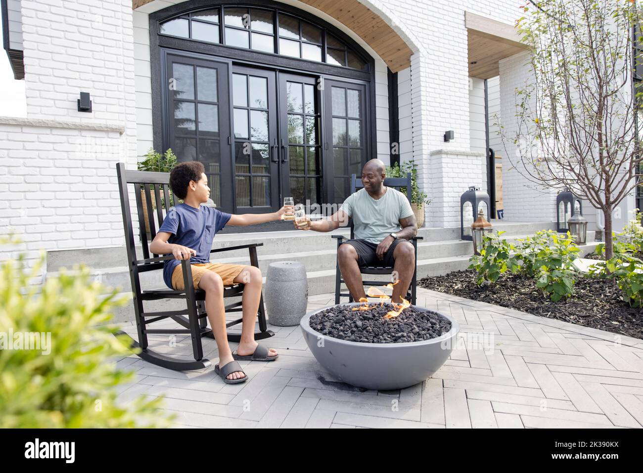 Father and son toasting water glasses at fire pit on patio Stock Photo