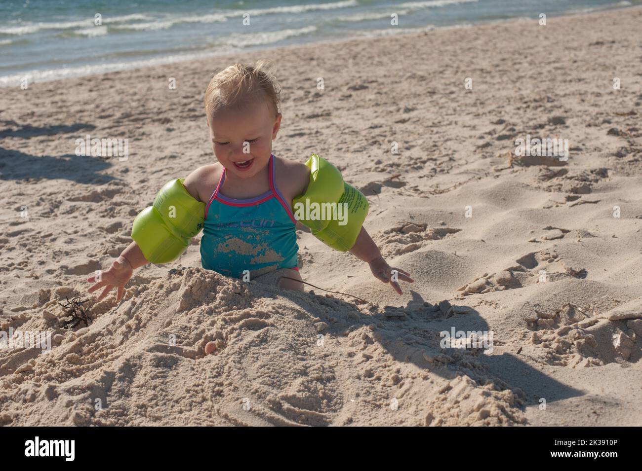 A toddler uncovers her toes after having her legs burried in sand at