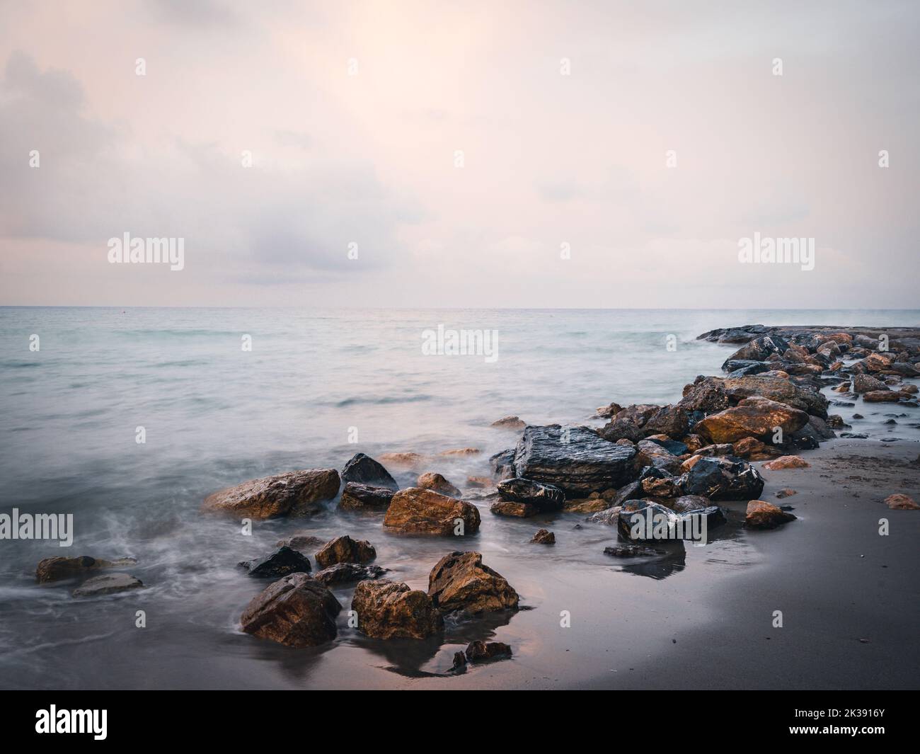 The sea waves calmly hitting a sandy beach with stones Stock Photo - Alamy