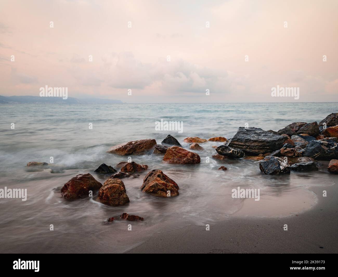 The sea waves calmly hitting a sandy beach with stones Stock Photo - Alamy