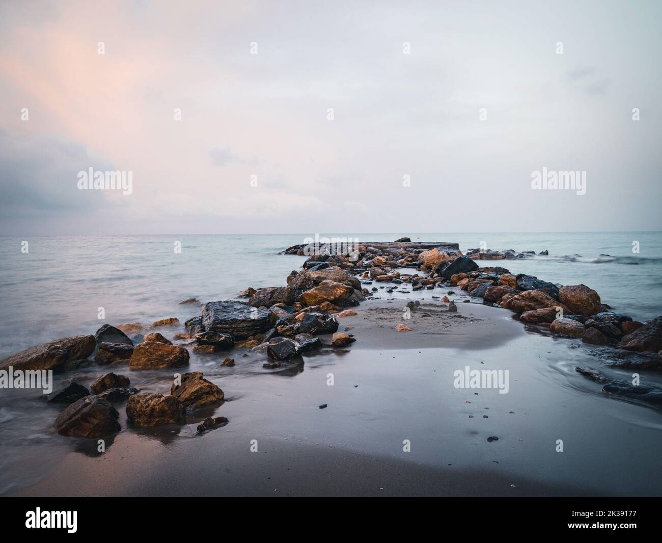 The sea waves calmly hitting a sandy beach with stones Stock Photo - Alamy