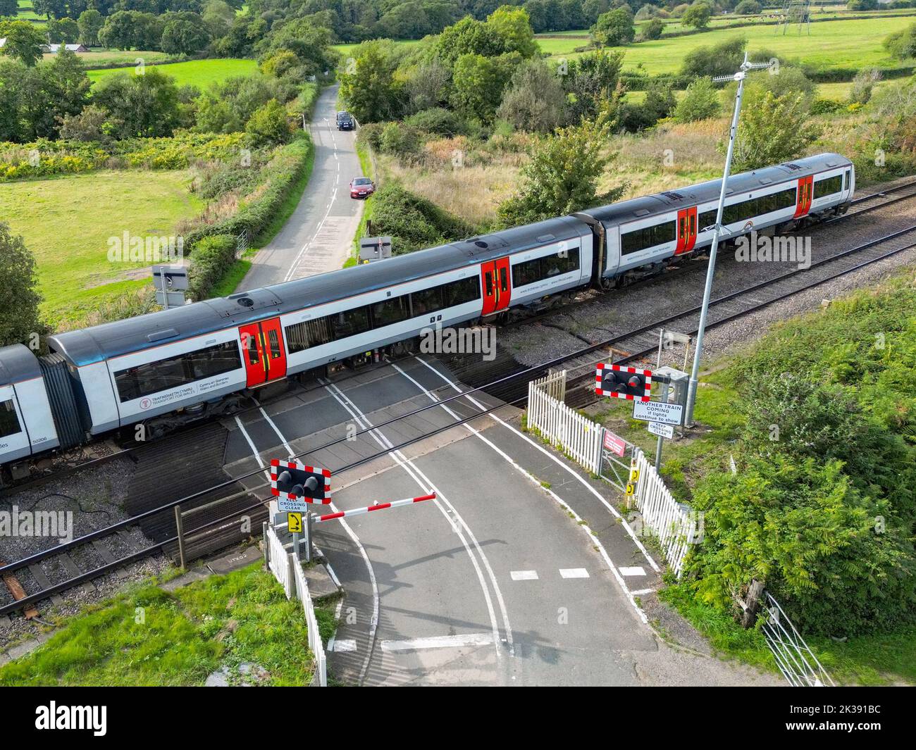 Bonvilston, Vale of Glamorgan, Wales - September 2022: Aerial view of a commuter train passing a level crossing on the outskirts of Cardiff. Stock Photo