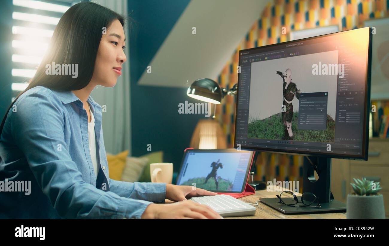 Asian female 3D designer creating visualization and animation for video game character while working on 3D project using pc and digital tablet computer Stock Photo