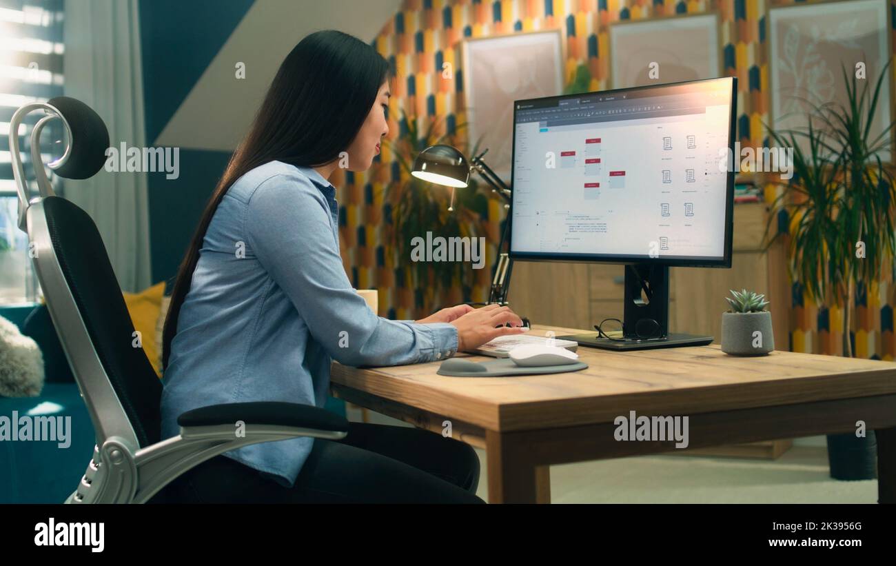 Female asian web designer using personal computer for creating website in professional constructor while working on project remotely at home. Freelance Stock Photo