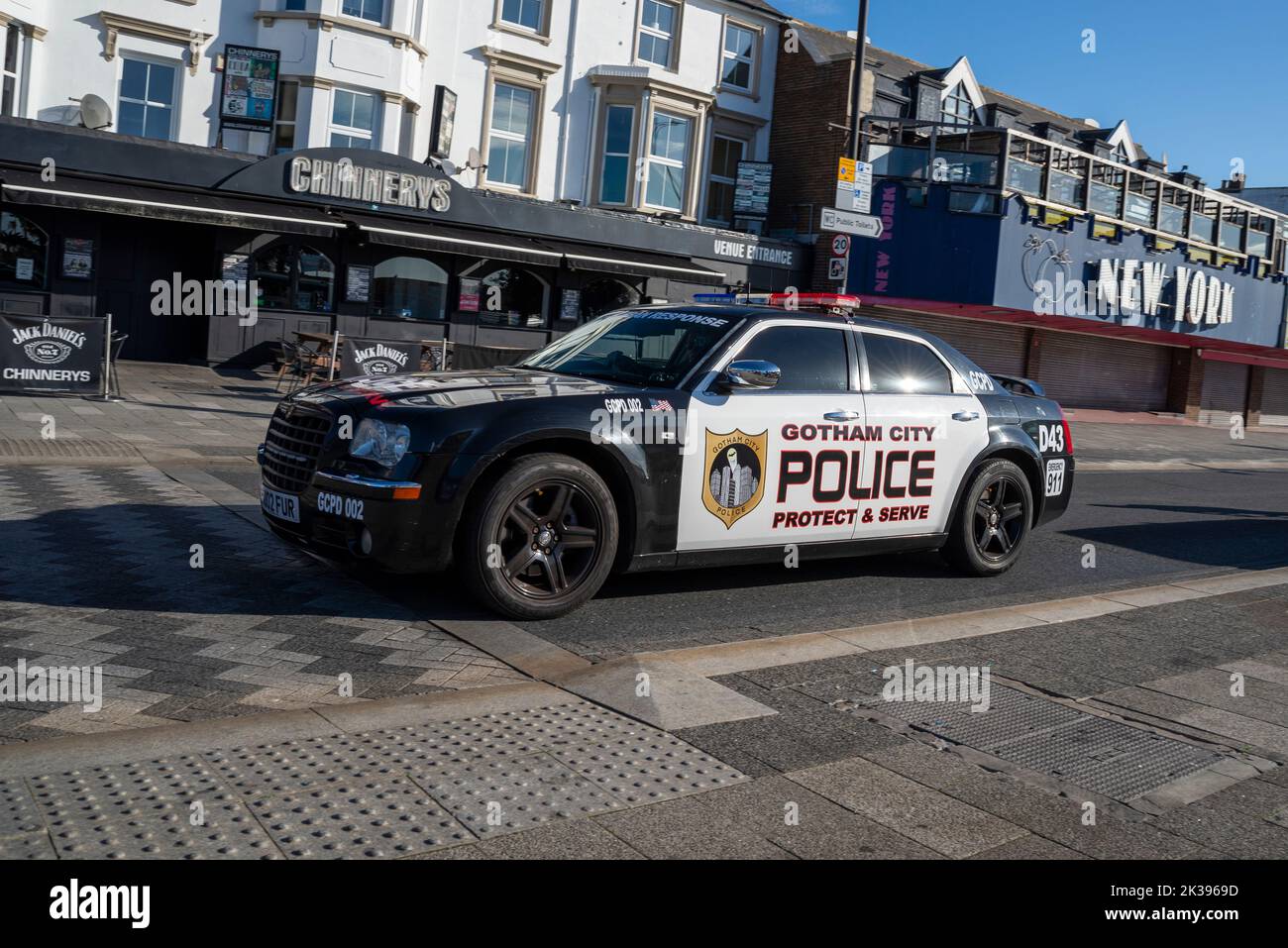 Gotham City police car marked Chrysler 300 driving on Marine Parade in Southend on Sea, Essex, UK. Protect & serve slogan. Passing New York arcade Stock Photo