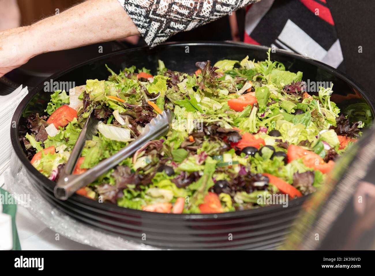Spring mix salad on the buffet table for guests to serve themselves with the tongs. Stock Photo