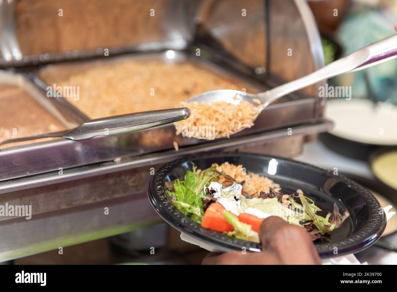 Party guest at the buffet line has a spoon full of Mexican rice to add to the plate of lunch food. Stock Photo