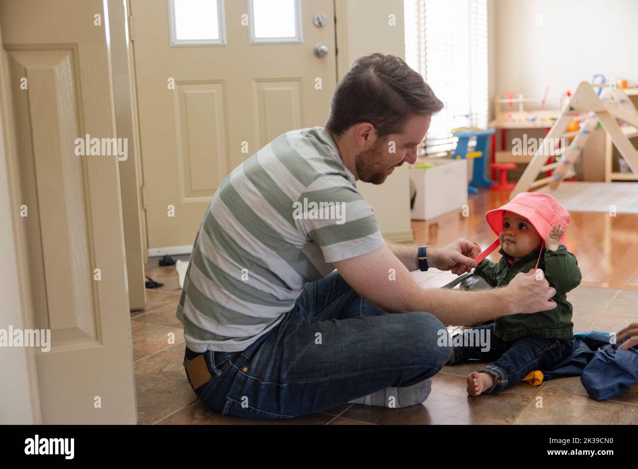Father putting hat on baby daughter in foyer Stock Photo Alamy