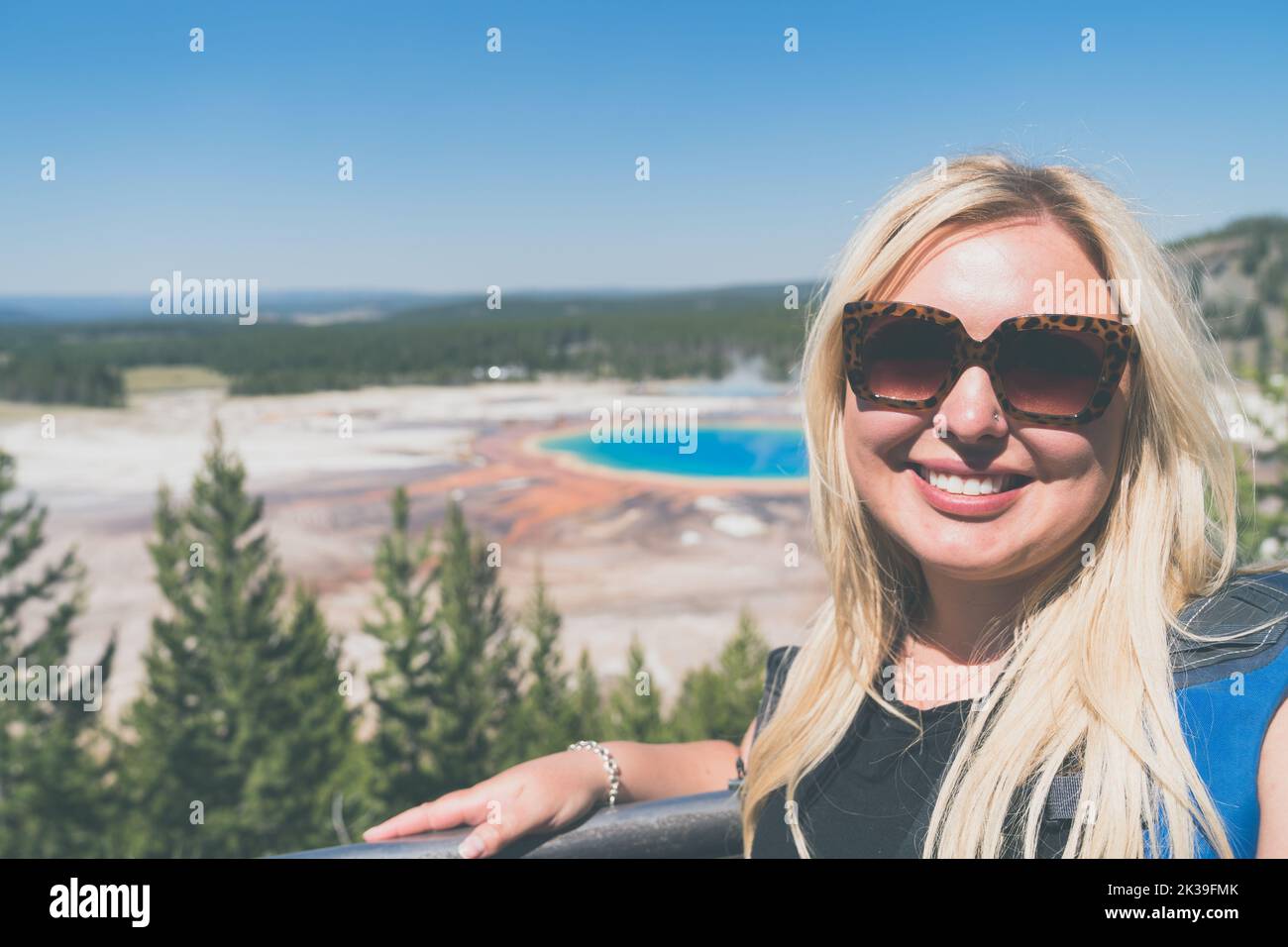 Pretty blonde woman smiles and poses at the overlook for Grand Prismatic Spring in Yellowstone National Park Stock Photo