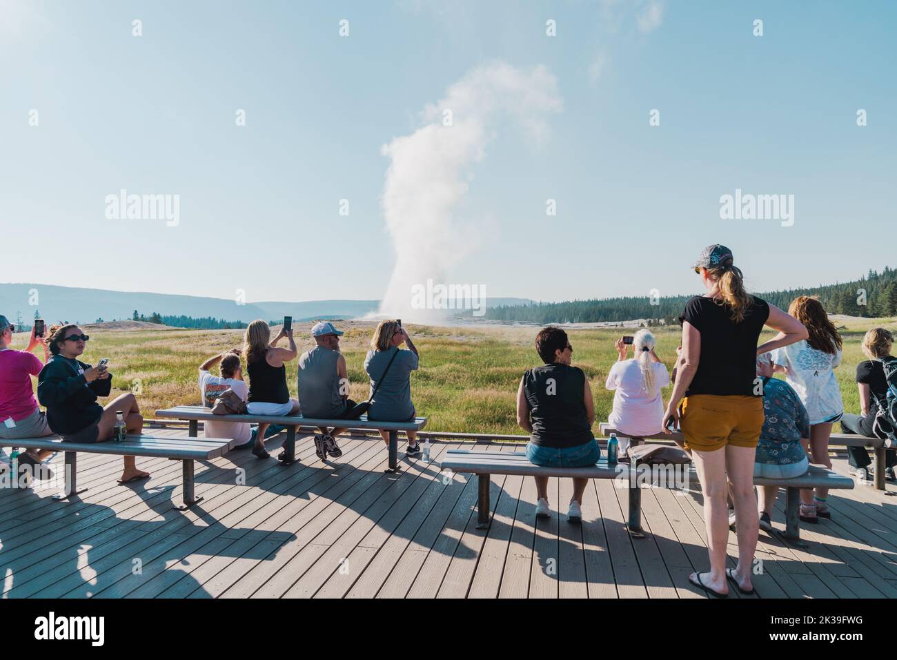 Wyoming, USA - July 19, 2022: Tourists watch Old Faithful geyser erupt from the boardwalk viewing area Stock Photo
