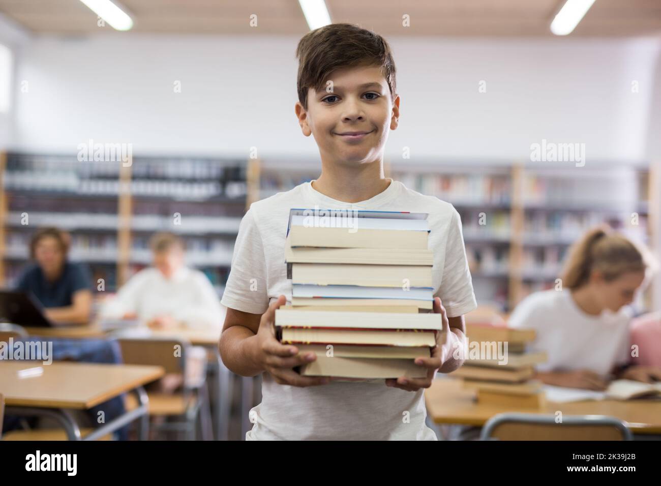 Teenager boy standing with a stack of books in library Stock Photo