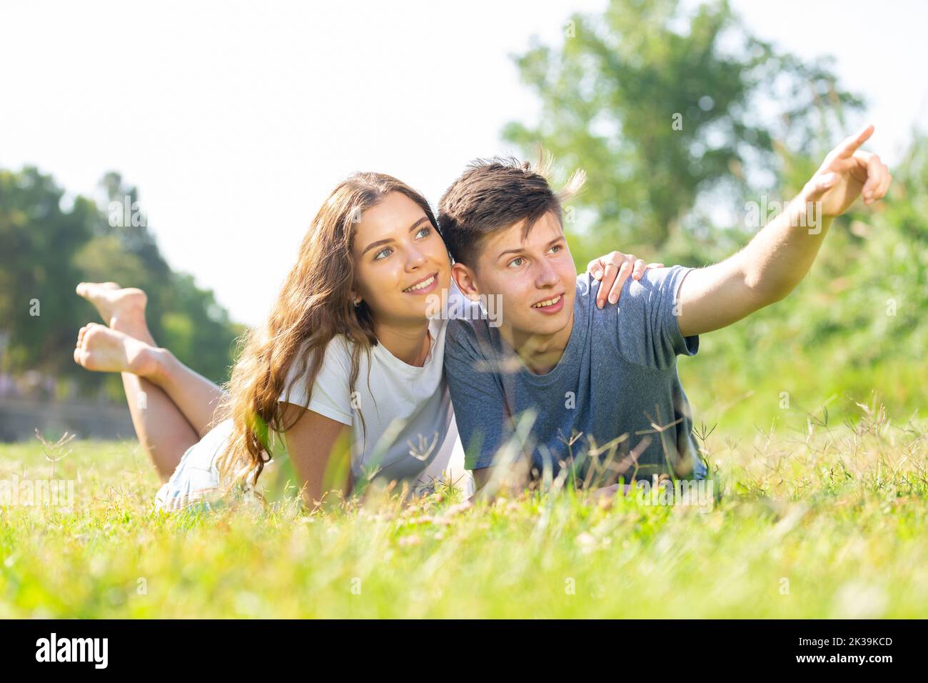 Happy couple lie on grass point with hand to something Stock Photo - Alamy