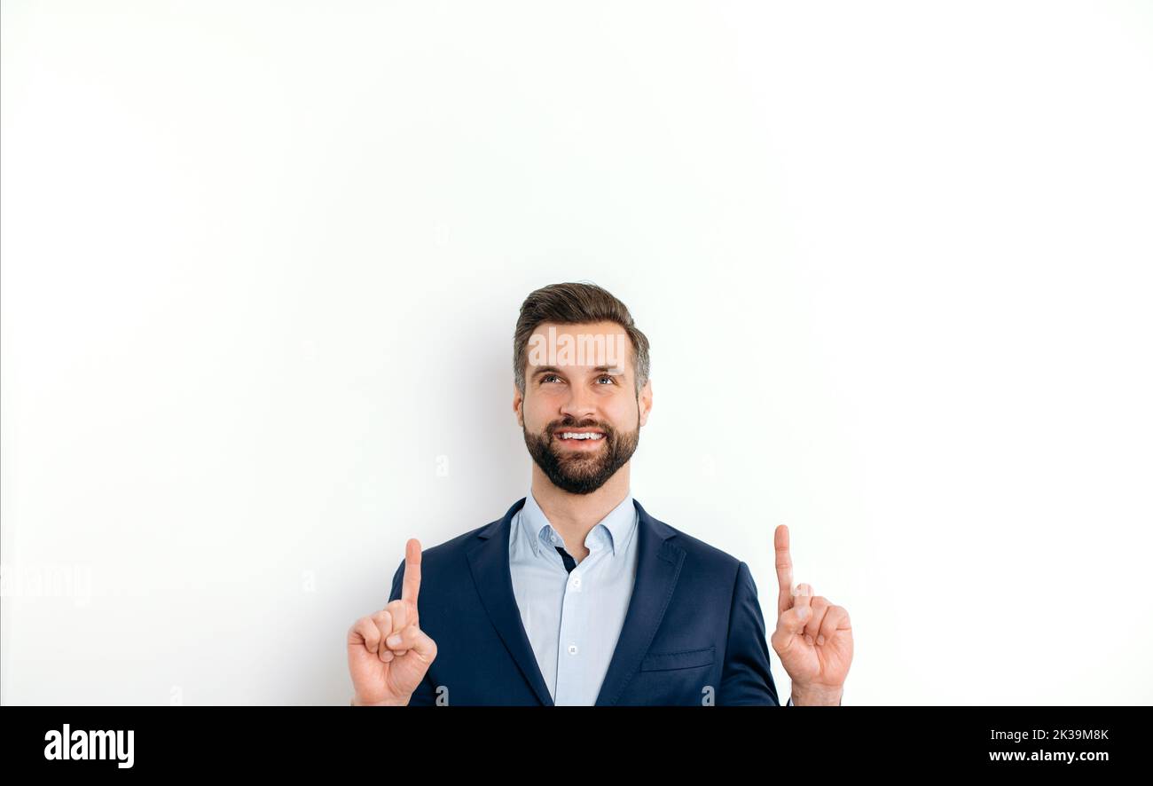 Positive attractive caucasian man, in elegant suit, pointing up with fingers hands gesture at empty space for presentation or advertising, stand on isolated white background, looks up, smiles Stock Photo
