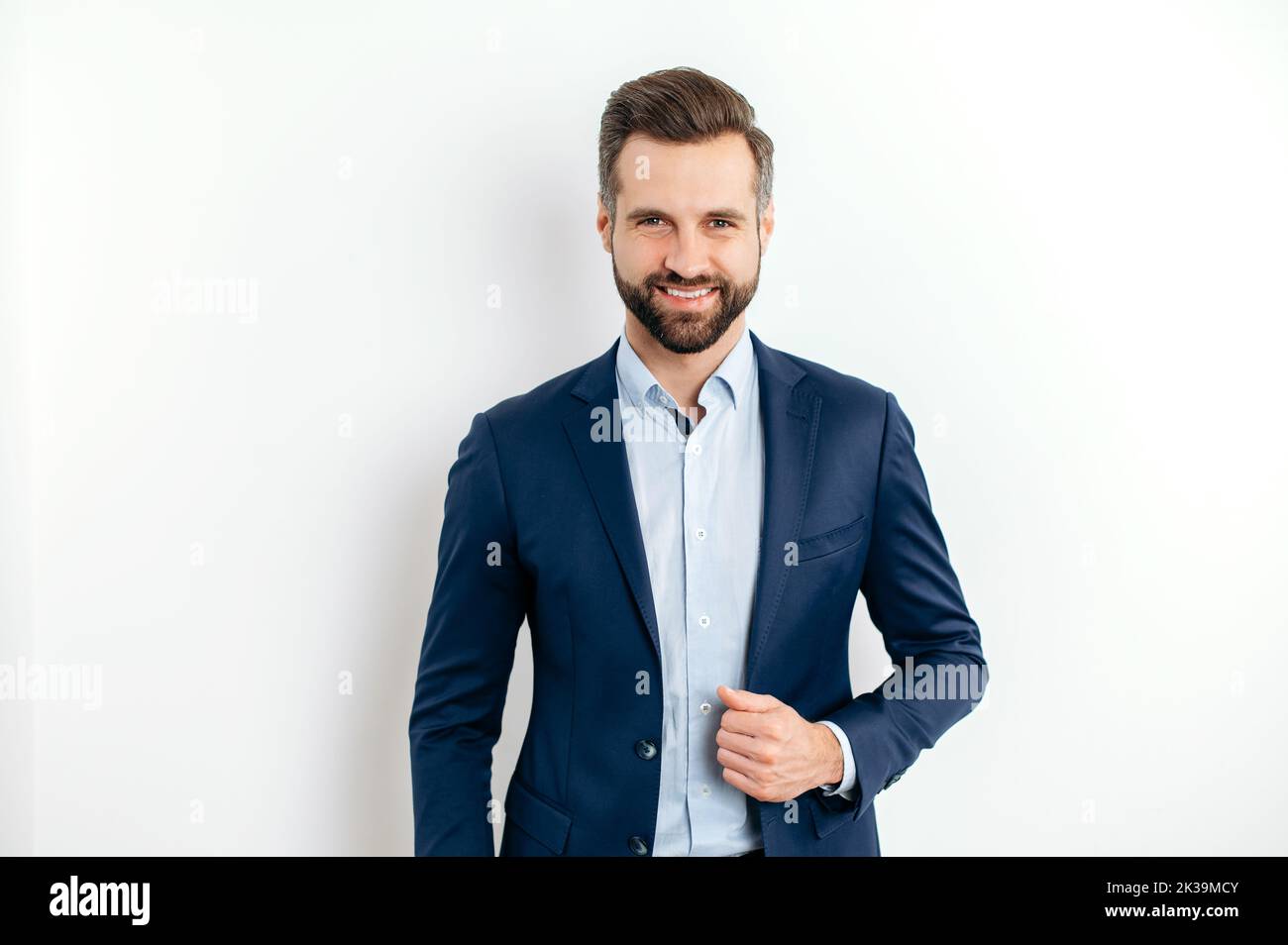 Portrait of a proud confident handsome bearded caucasian businessman, successful ceo, in formal elegant suit, standing on isolated white background, looking at the camera, smiling friendly Stock Photo