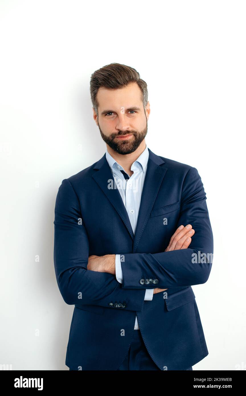 Vertical photo of a proud confident handsome bearded caucasian businessman, corporate executive, in formal elegant suit, stand on isolated white background with arms crossed, looks at camera, smiling Stock Photo