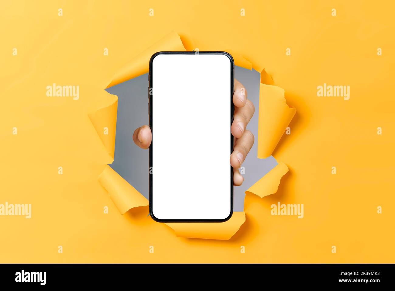 Male hand showing smartphone with blank white mock up screen through hole in ripped orange paper background. Mockup for app, advertising or presentation. Copy-space concept Stock Photo