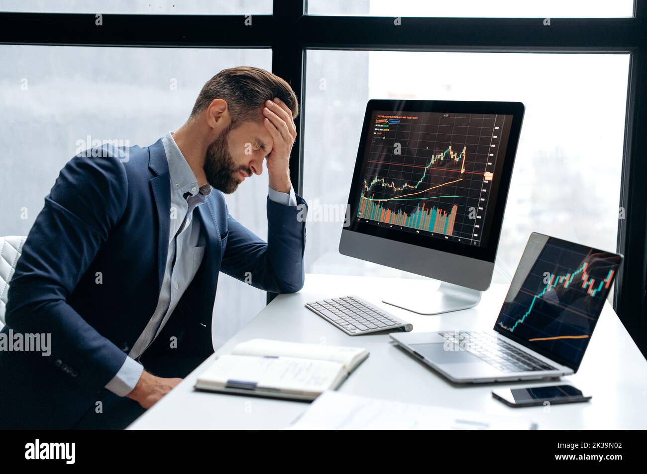 Upset stressed worried caucasian male stock investor, broker, financial expert, sit at work desk in front of computer with charts, nervous of fall cryptocurrency coin, closed eyes, disappointment Stock Photo