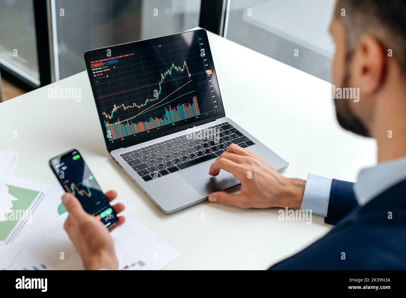 Caucasian crypto trader investor using cellphone and laptop for cryptocurrency financial market analysis, buying or selling cryptocurrency.Close-up of laptop and smart phone screen with stock diagrams Stock Photo