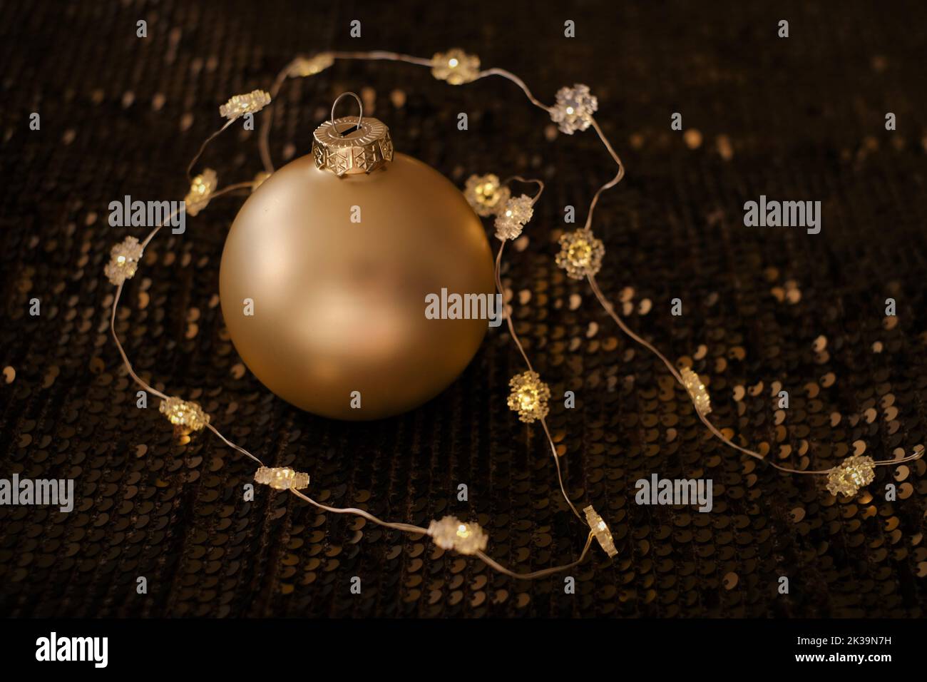 Golden balls and glowing garlands on brown sequins background.Christmas balls background.Festive background in Gold and brown tones. Stock Photo