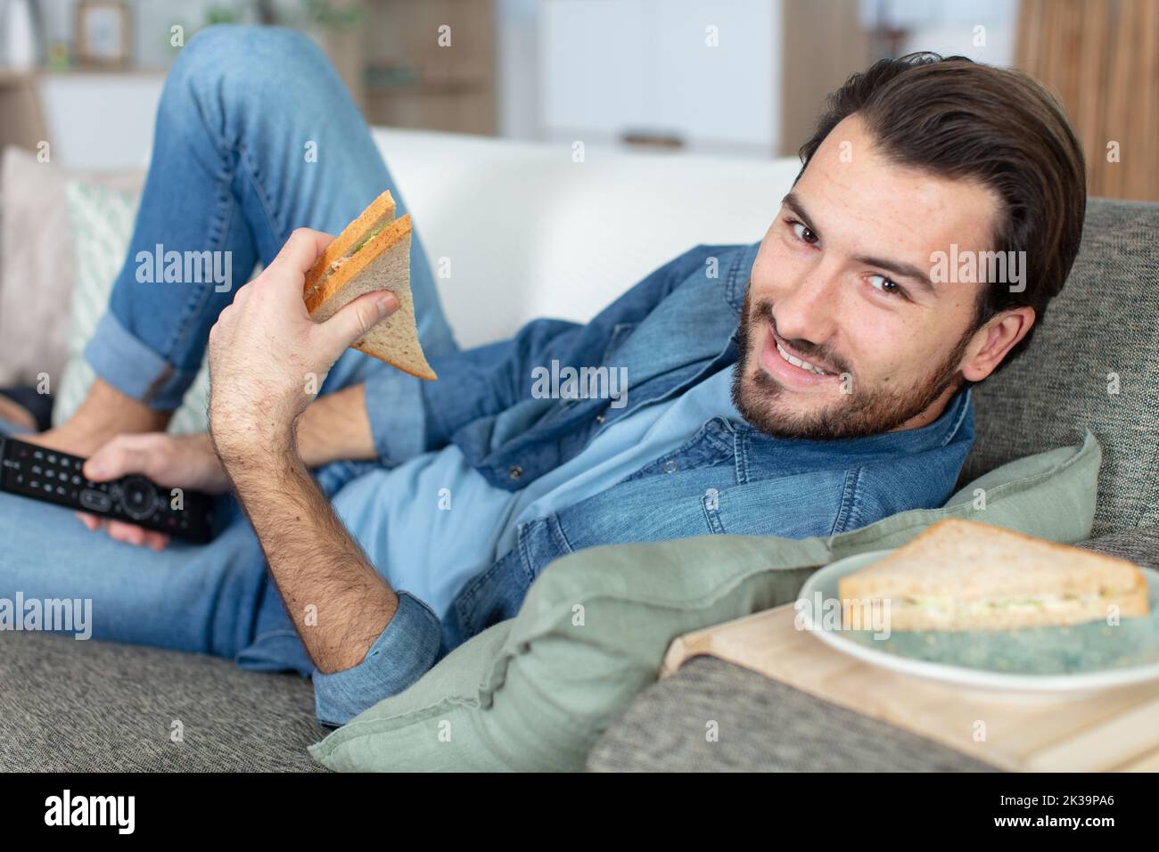 man laying on sofa eating a sandwich Stock Photo Alamy