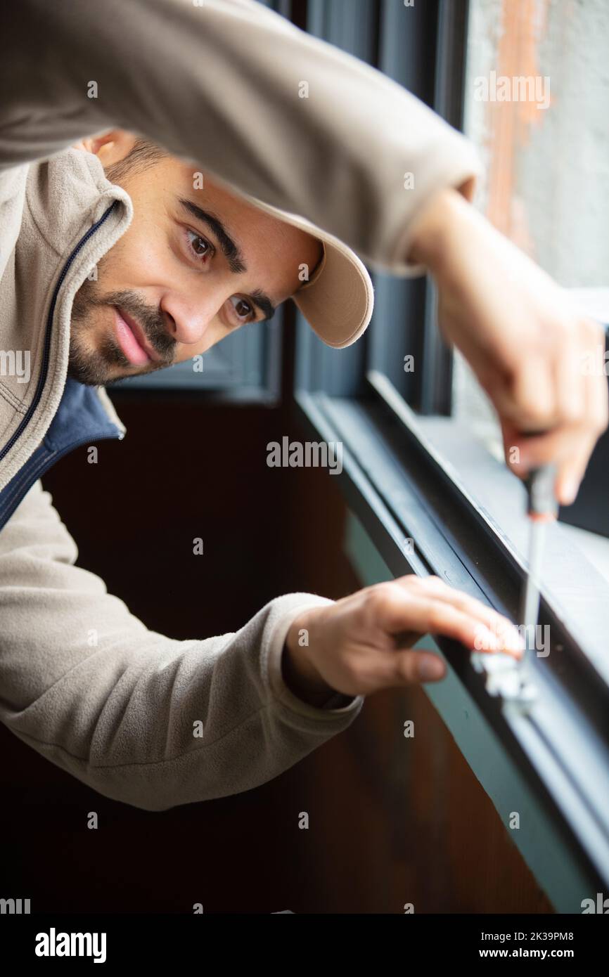construction worker repairing plastic window with screwdriver indoors Stock Photo