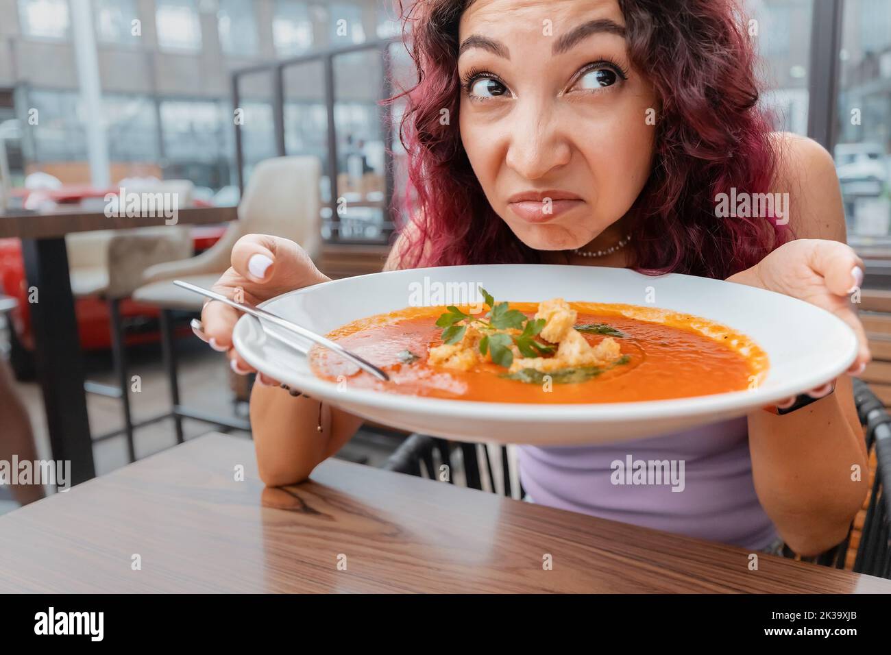 A woman dissatisfied customer of the restaurant sniffs the disgusting smell of a bowl of soup with spoiled ingredients and is going to complain to the Stock Photo