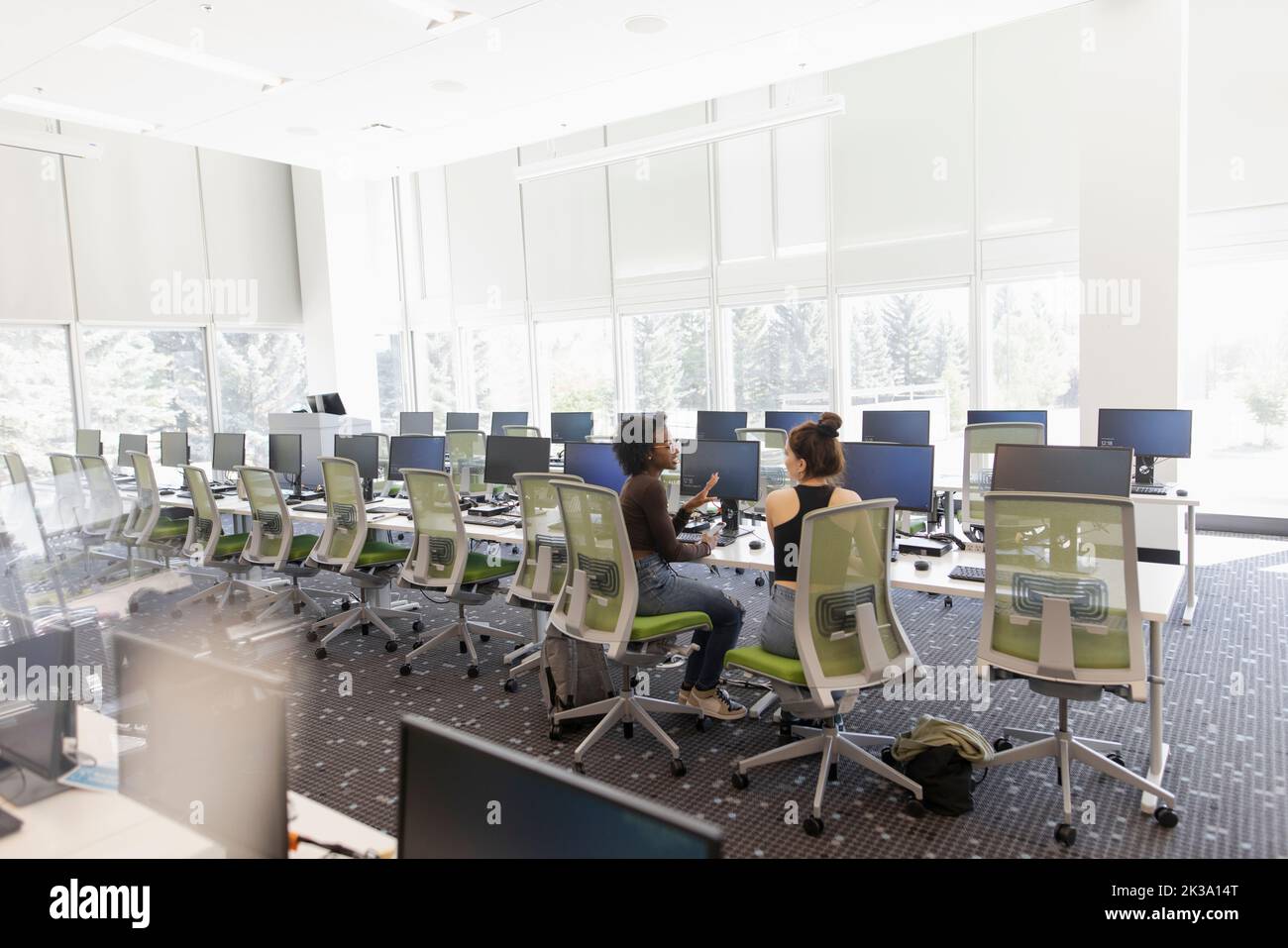 Young female college students talking at computers in computer lab ...