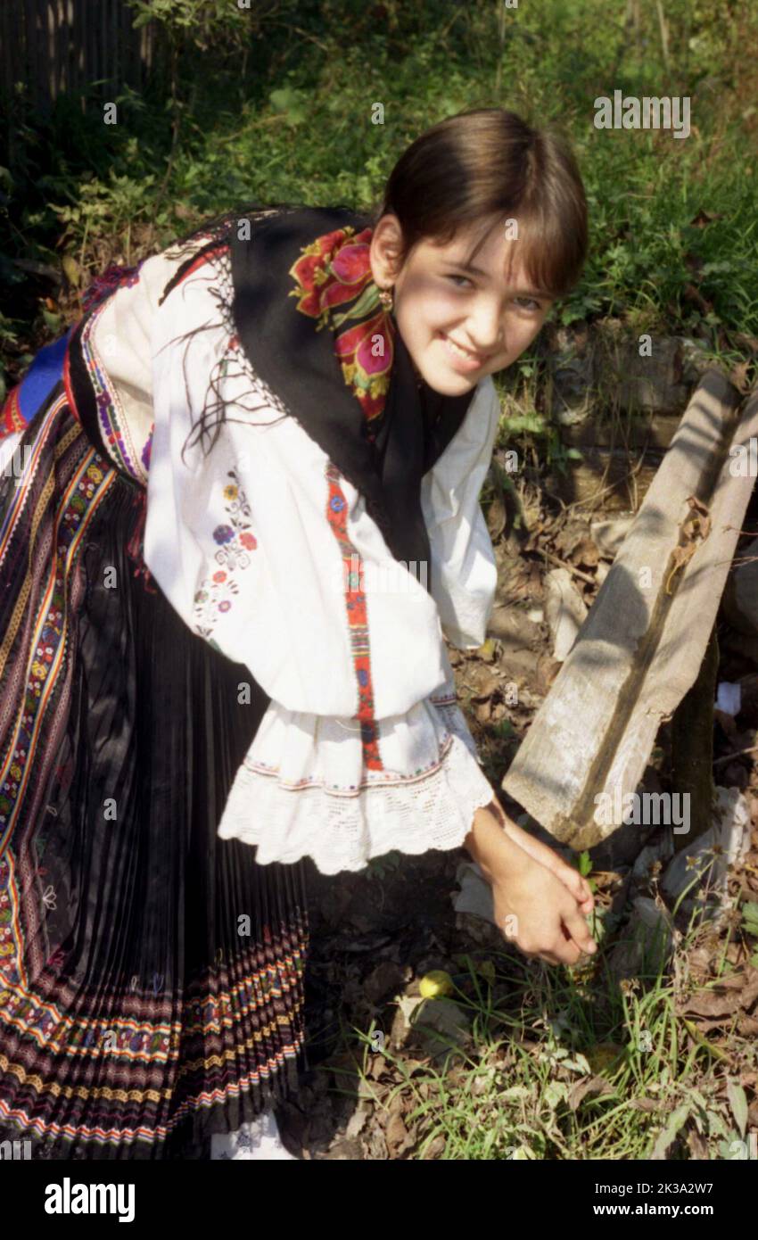 Poșaga, Alba County, Romania, approx. 1999. Young girl wearing the traditional costume washing her hands at a water spout. Stock Photo