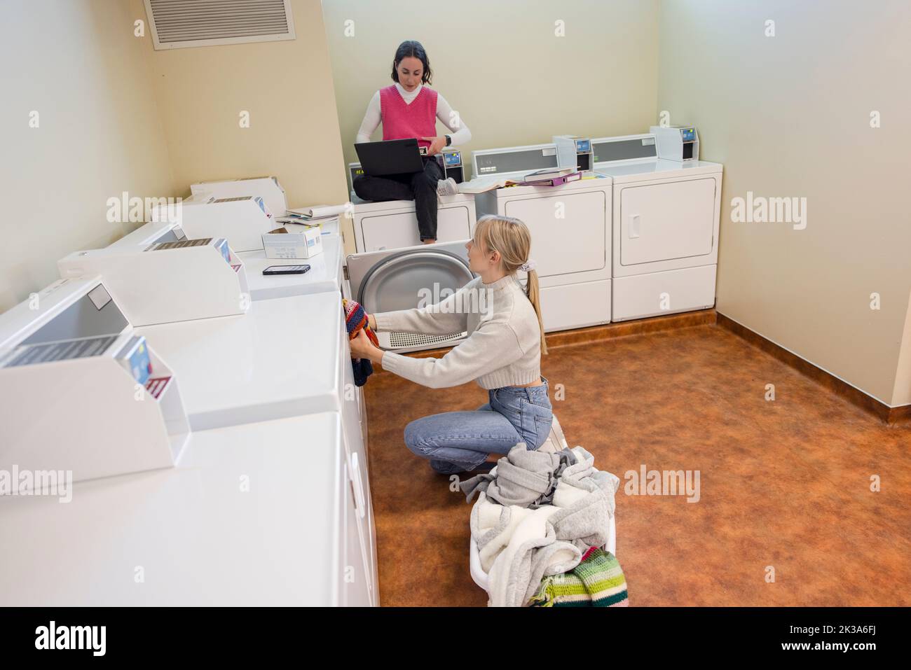Young female college students doing laundry in dormitory laundry room