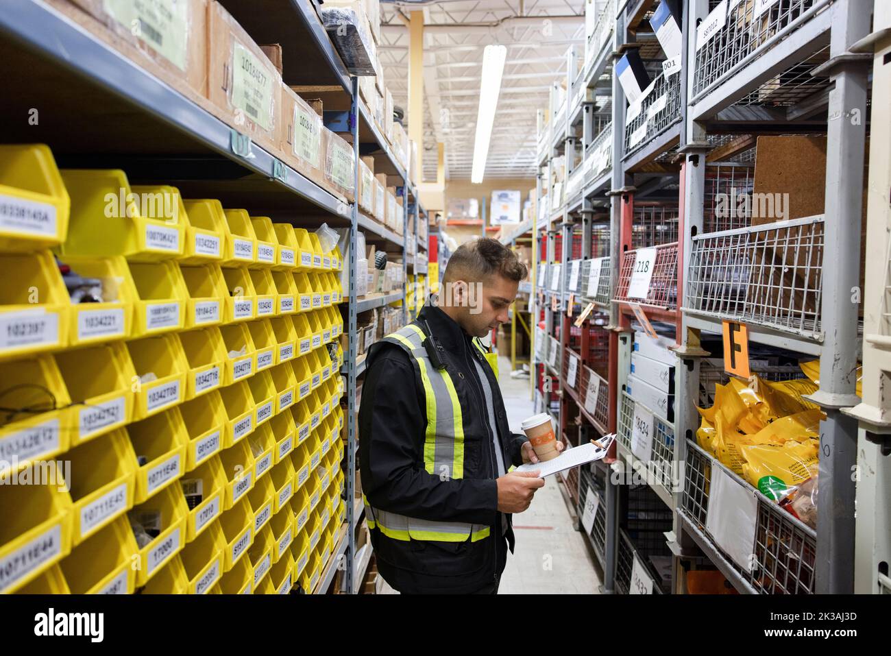 Worker with hot drink looking at checklist in distribution warehouse ...