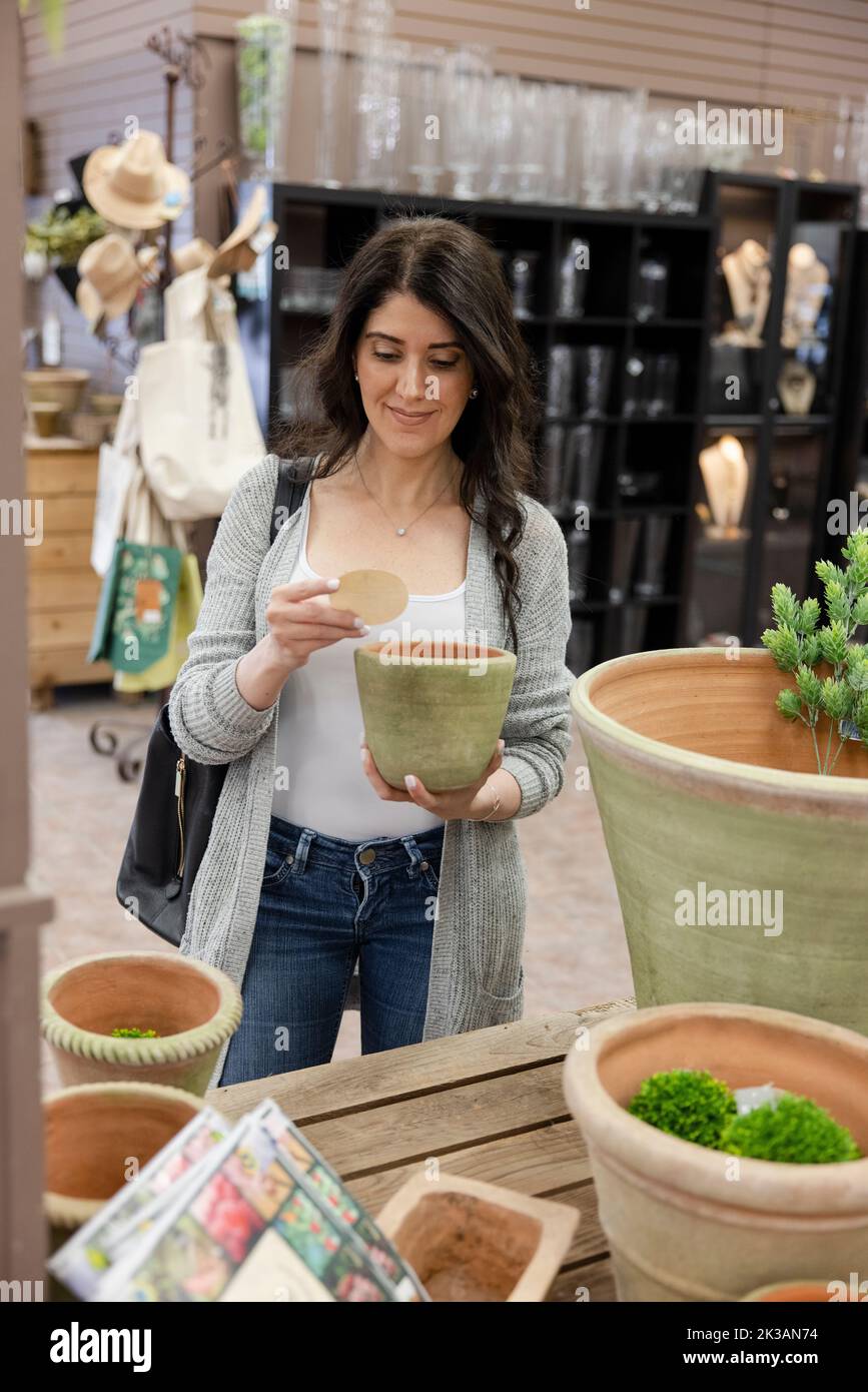 Cheerful customer looking at price tag of plant pot in garden center Stock Photo