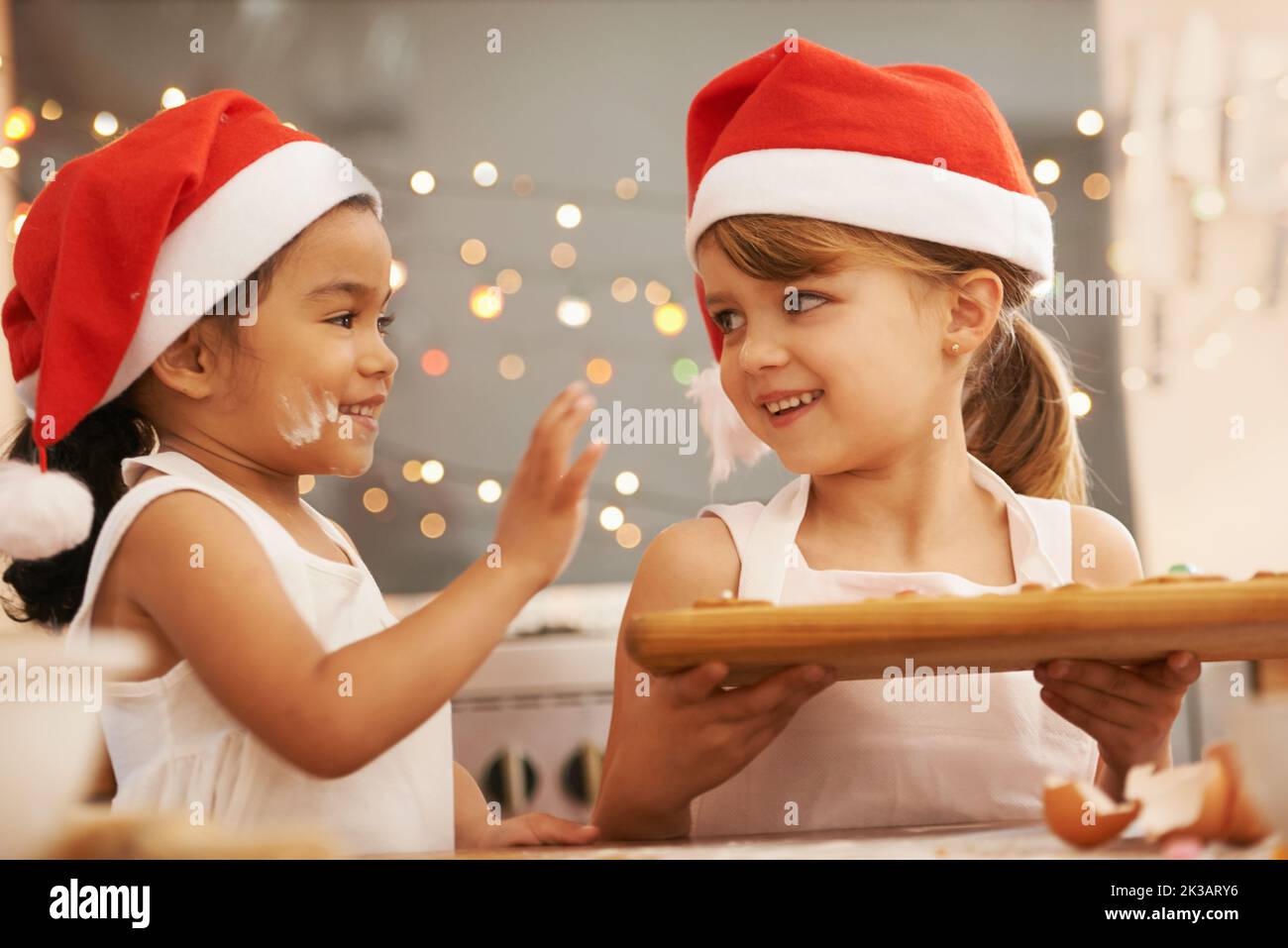 Playful bakers. Two little girls wearing santa hats baking in the kitchen. Stock Photo