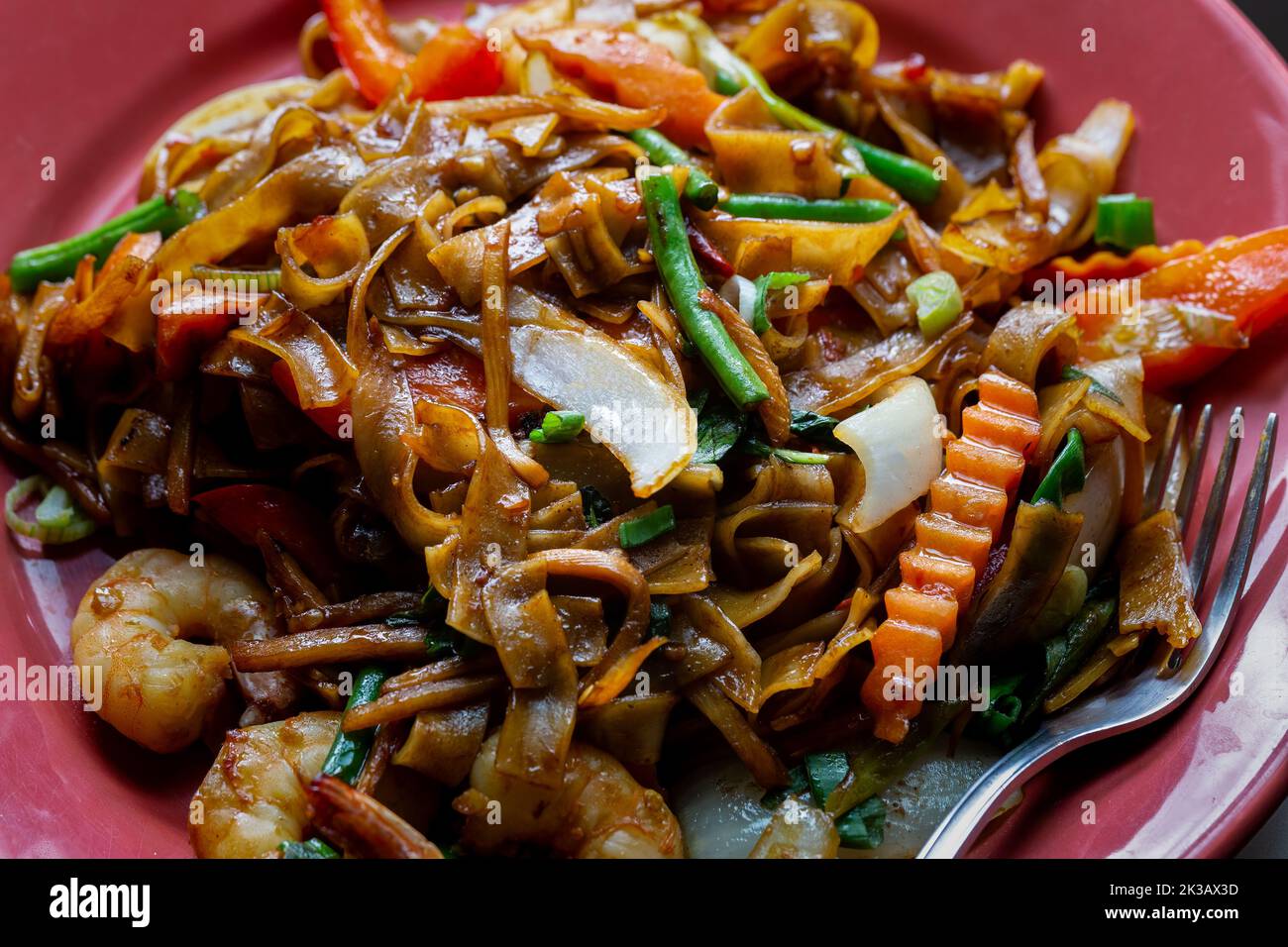 Drunken noodles, pad kee mao, with prawns, basil, chilii, peppers and green beans. Close-up on a plate. Stock Photo