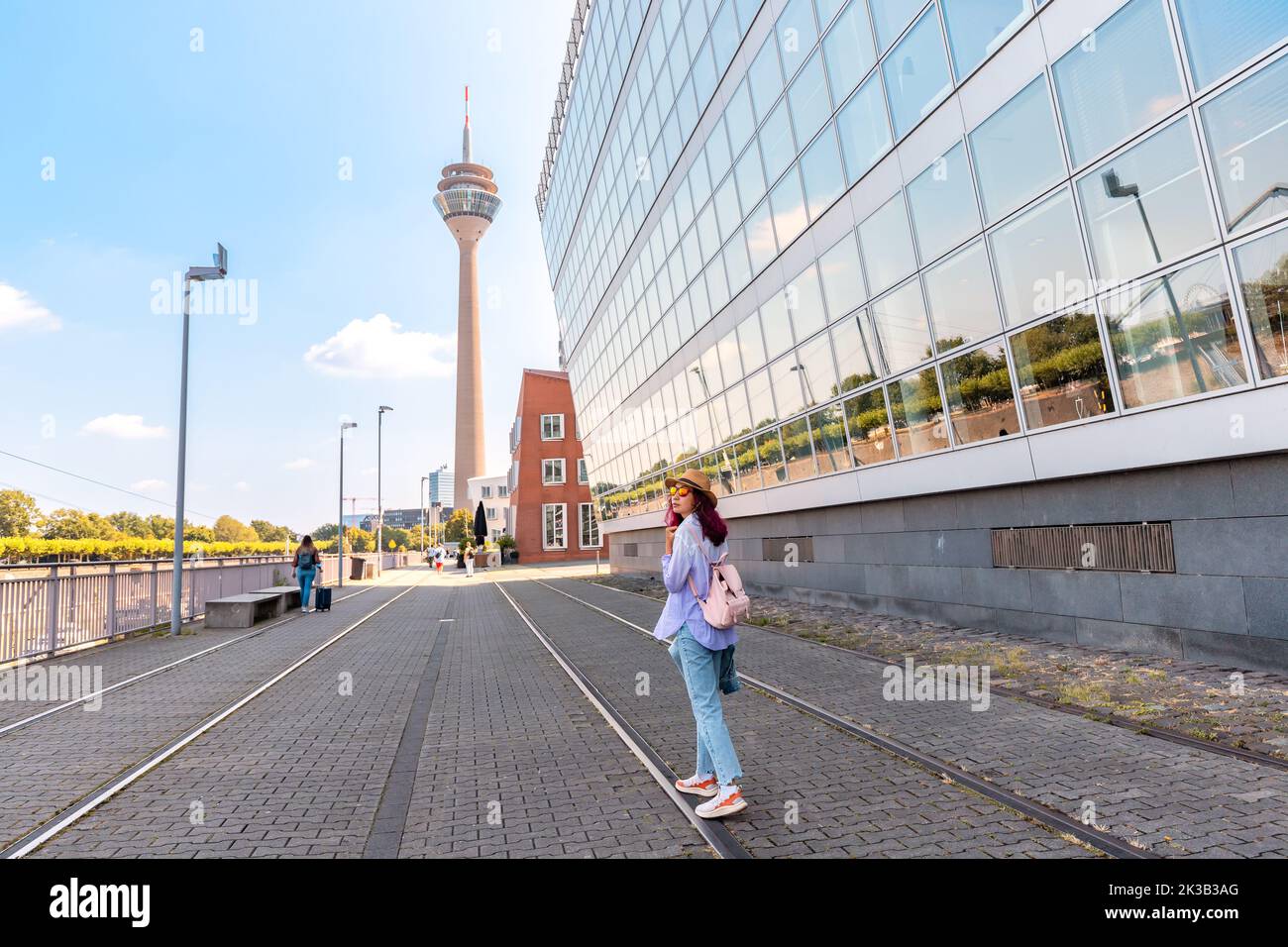 Asian girl traveler enjoys a beautiful view in the Media Bay during a tourist trip or a student education in Dusseldorf. Rheinturm TV Tower in the bac Stock Photo
