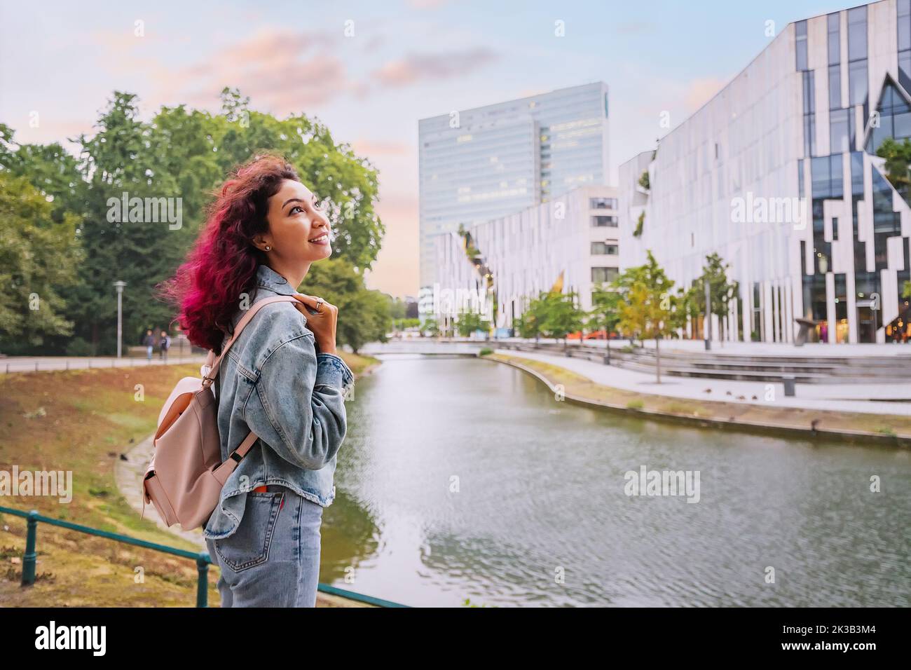 Happy tourist woman with backpack visiting Konigsallee water channel and admiring great modern architecture buildings in Dusseldorf, Germany Stock Photo