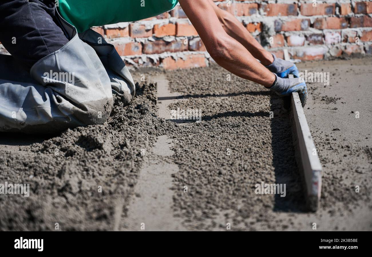 Close up of man builder placing screed rail on the floor covered with