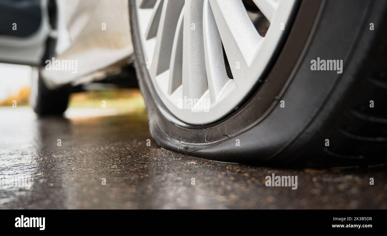 Close-up view of punctured, flat tire on rear wheel of automobile. Fault, damage wheel while driving on asphalt road. Bad luck, accident concept. Stock Photo