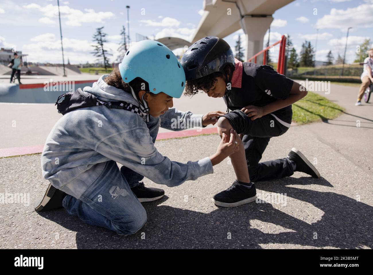 Boy checking brother's injured knee in skatepark Stock Photo