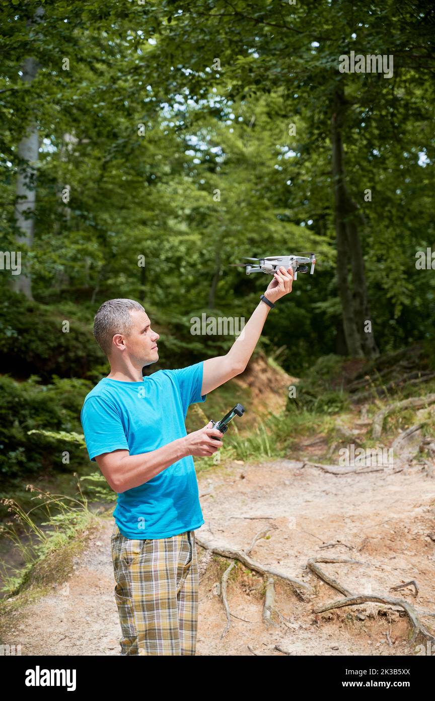 Man operating drone using remote controller. Man using drone for photos and video making while standing in green forest. Stock Photo