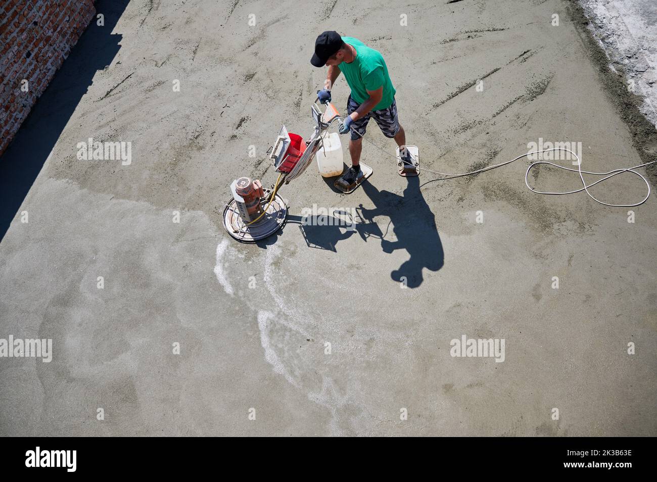 Aerial view of man builder using troweling machine while screeding floor on the roof of residential building. Worker finishing concrete surface with floor screed grinder machine at construction site. Stock Photo